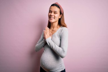 Genç ve güzel bir kız hamile. Pembe arka planda bir bebek bekliyor. Birlikte dua ediyoruz..