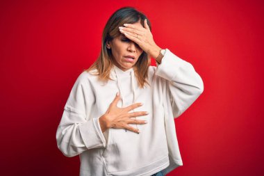 Orta yaşlı, güzel bir sporcu kadın izole edilmiş kırmızı arka plan üzerine gündelik bir kazak giyiyor. Hastalık, ateş, grip ve soğuk algınlığı için alnına dokunuyor.