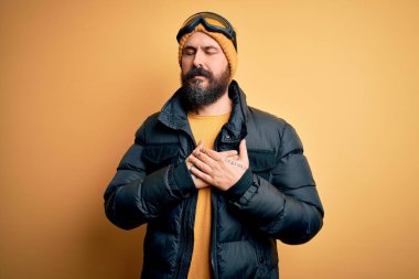 Sakallı, kar maskesi takmış, kar maskesi takmış, elleri göğsünde, gözleri kapalı ve yüzünde minnet dolu bir jest olan yakışıklı bir kayakçı. Sağlık kavramı.