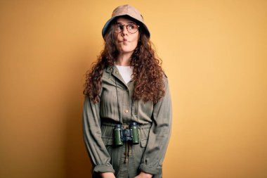 Gezgin şapkası ve dürbünle gezen genç ve güzel bir turist kadın dudaklarıyla balık suratı yapıyor, çılgınca ve komik bir jest. Komik ifade.