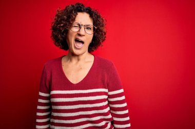 Orta yaşlı, kıvırcık saçlı, sıradan çizgili süveter giyen, kırmızı arka planda yanıp sönen, seksi bir ifadeyle kameraya bakan, neşeli ve mutlu yüzlü bir kadın..