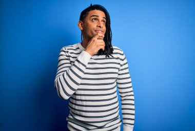 Rasta desenli çizgili süveter giyen, eli çenesinde soru soran, düşünceli bir Afro-Amerikan genç adam. Gülen ve düşünceli bir yüz. Şüphe kavramı.