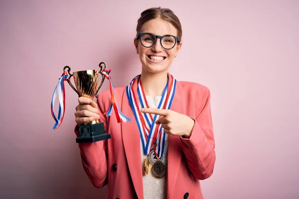 Jovem Bela Ruiva Segurando Troféu Vestindo Medalhas Sobre Fundo Rosa — Fotografia de Stock