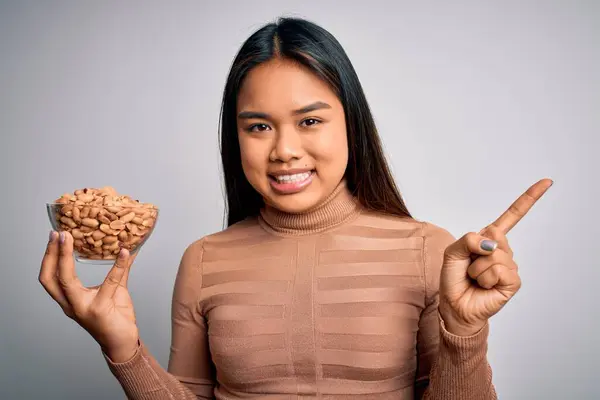 Genç Asyalı Kız Elinde Sağlıklı Fıstık Kasesi Bembeyaz Arka Planda — Stok fotoğraf