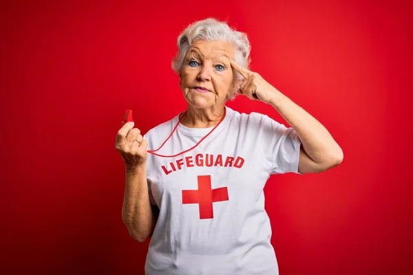 シニア美しい白髪のライフガード女性を着てTシャツ赤い十字を使用して笛1本の指で頭を指して笑顔 素晴らしいアイデアや考え 良い記憶 — ストック写真