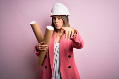 Güvenlik kaskı takan genç ve güzel mimar kadın elinde kamerayı işaret eden planlar ve sen, el işareti, ön taraftan pozitif ve kendinden emin bir jest.