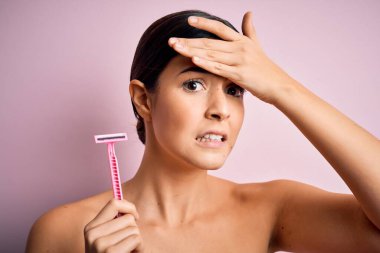 Young beautiful girl using shaver for depilation standing over isolated pink background stressed with hand on head, shocked with shame and surprise face, angry and frustrated. Fear and upset for mistake. clipart