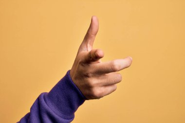 İzole edilmiş sarı arka plan üzerinde parmaklarını gösteren beyaz bir genç adamın eli kamerayı işaret ediyor ve yönü gösteriyor.