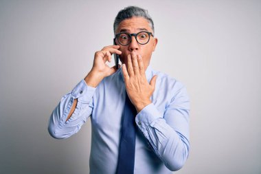 Orta yaşlı, yakışıklı, gri saçlı iş adamı akıllı telefondan konuşuyor, ağzı kapalı, utancından ağzı açık bir şekilde konuşuyor, korku ifadesi, sessizlikten korkuyor, gizli bir konsept.