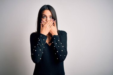 Mavi gözlü, beyaz arka planda siyah süveter giyen esmer kadın ağzını yanlışlıkla elleriyle kapatmış. Gizli konsept.