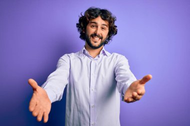 Mor arka plan üzerinde duran sakallı yakışıklı iş adamı kameraya sarılmak için gülümseyerek bakıyor. Mutluluğu kucaklayan neşeli bir ifade..