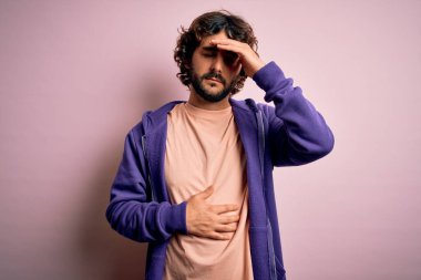 Sakallı, pembe arka planda sıradan bir kazak giyen yakışıklı genç bir adam. Hastalık, ateş, grip, soğuk algınlığı ve virüs yüzünden alnına dokunuyor.