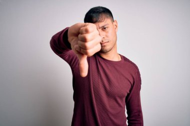 Beyaz izole edilmiş arka plan üzerinde duran sıradan tişörtlü, genç, yakışıklı İspanyol bir adam mutsuz, reddedilmiş ve olumsuz jestler yapıyor. Kötü ifade.
