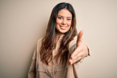 Genç, güzel, esmer bir kadın beyaz arka planda dikilip gülümseyerek selamlama ve hoş geldin diyor. Başarılı bir iş..