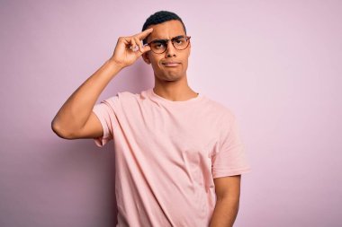 Yakışıklı Afro-Amerikalı adam pembe arka planda günlük tişört ve gözlük takıyor. Alnındaki sorun yüzünden endişeli ve stresli.