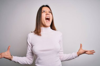 Genç ve güzel esmer bir kız, sıradan bir süveter giyip izole edilmiş beyaz arka planda duruyor. Deli deli deli bağırıyor ve bağırıyor. Agresif bir ifade ve kollar havada. Hayal kırıklığı konsepti.