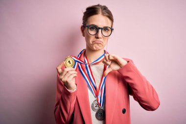 Genç, güzel, kızıl saçlı bir kadın, izole edilmiş kırmızı arka planda madalyalar takıyor. Kızgın bir yüzü var. Negatif işaretleri var.