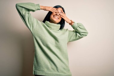 İzole edilmiş arka planda yeşil süveter giyen genç, İspanyol bir kadın. Gözleri neşeli ve komik gülümseyerek kapatıyor. Kör kavram.