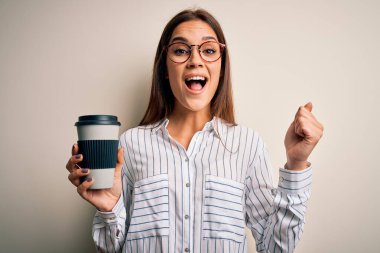 Genç güzel esmer kadın beyaz arka planda bir fincan kahve içerek gururla bağırıyor ve zaferi ve başarıyı kutluyor. Çok heyecanlı, coşkulu bir duygu.