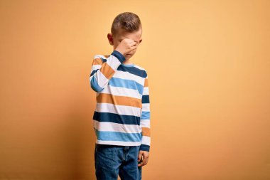 Mavi gözlü, sarı arka plan üzerinde çizgili gömlek giyen, burnu ve gözleri ovuşturan yorgun, bitkin ve baş ağrısı çeken küçük beyaz bir çocuk. Stres ve hüsran kavramı.