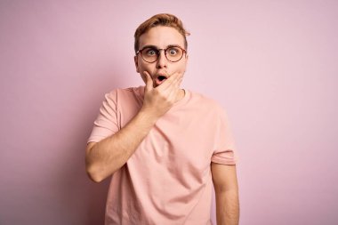 İzole edilmiş pembe arka planda duran sıradan tişörtlü genç, yakışıklı kızıl saçlı adam, elleri çenesinde olan inançsızlıktan, şaşkınlıktan ve şaşkınlıktan büyülenmiş görünüyor.