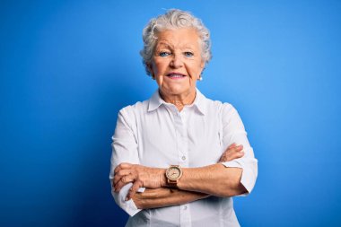 Soyutlanmış mavi arka planda duran zarif tişört giyen, kollarını kavuşturup kameraya bakan son derece güzel bir kadın. Pozitif kişi.