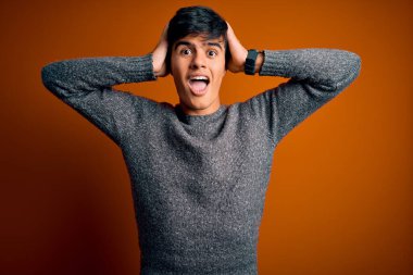 Yalnız turuncu arka planda dikilen genç ve yakışıklı bir adam elleri başının üstünde korkmuş, korkmuş ve ağzı açık şoktan şaşırmış.