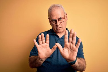 Sarı arka plan üzerine gündelik polo ve gözlük takan orta yaşlı, yakışıklı beyaz bir adam. Avuçlarını kaldırıyor, reddediyor ve iğrenç bir ifadeyle reddediyor. Dur ve yasakla.