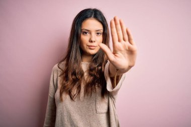 Genç, güzel, esmer bir kadın pembe arka planda dikilip avucuyla şarkı söylemeyi kesiyor. Yüzünde olumsuz ve ciddi bir jest olan uyarı ifadesi.