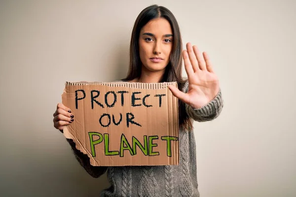 Young beautiful brunette activist woman protesting for protect our planet holding poster with open hand doing stop sign with serious and confident expression, defense gesture