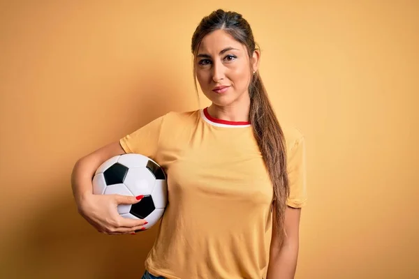 美しいブルネットプレーヤー女性遊びサッカーボールを使用して黄色の背景に自信を持って表現上のスマート顔考え深刻な — ストック写真