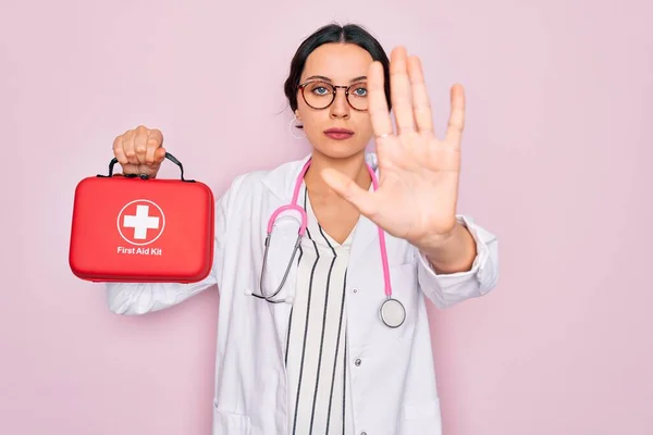 Young beautiful doctor woman with blue eyes wearing stethoscope holding first aid kit box with open hand doing stop sign with serious and confident expression, defense gesture