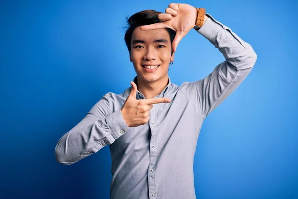 若いハンサムな中国人男性が幸せな顔を持つ手と指でフレームを作る独立した青の背景笑顔の上に立ってカジュアルなシャツを着ている 創造性と写真の概念 — ストック写真