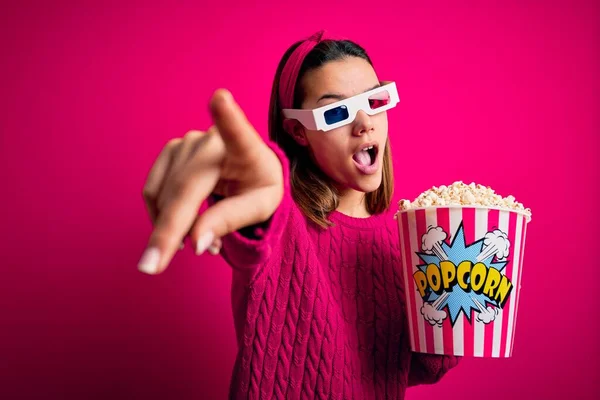 年轻美丽的女孩在看电影时 用3D眼镜吃着爆米花 手指指向前方 张开嘴惊讶的表情 前面有什么东西 — 图库照片