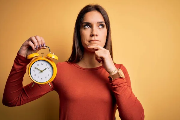 Jovem Bela Morena Segurando Despertador Sobre Fundo Amarelo Isolado Rosto — Fotografia de Stock