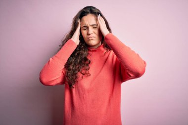 Kıvırcık saçlı, pembe arka plan üzerine balıkçı yaka kazak giyen, başı ağrıyan bir kadın. Stres yüzünden. Migren ağrısı..