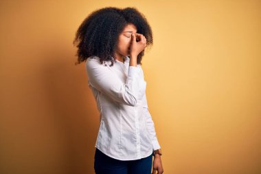 Afro saçlı, sarı arka planda duran, yorgun, burnu ve gözleri ovuşturan yorgun ve başı ağrıyan güzel, Afro-Amerikan zarif genç bir kadın. Stres ve hüsran kavramı.