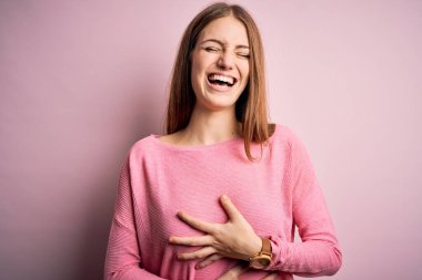 Genç, güzel, kızıl saçlı bir kadın, izole edilmiş mavi arka planda günlük süveter giyiyor, gülümsüyor ve kahkahalarla gülüyor..