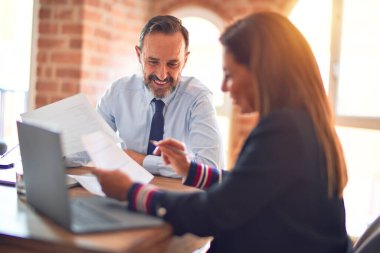 Mutlu ve kendinden emin gülümseyen iki orta yaşlı iş adamı. Ofiste dizüstü bilgisayarla gülümseyerek birlikte çalışıyoruz.