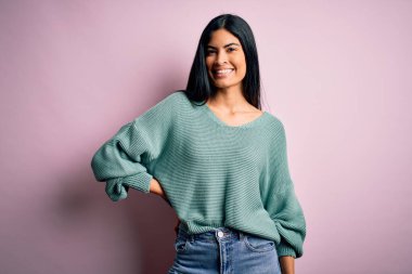 Moda kıyafetleri giyen genç ve güzel bir kadın. Manken, sokak tarzı giyiniyor. Pembe arka planda dikiliyor.