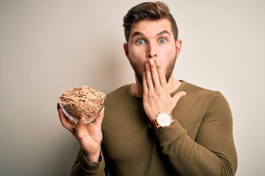 Sakallı, mavi gözlü, elinde mısır gevreğiyle kasesi olan genç, sarışın bir adam. Ağzını kapatıyor. Yanlışlıkla utancından ağzı açık kalıyor.