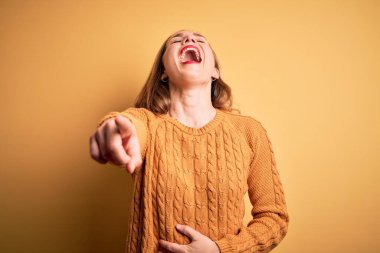 Sarı arka planda sıradan bir süveter giyen genç, güzel sarışın kadın sana gülüyor, kamerayı işaret ediyor, vücudunu gösteriyor, utanç ifadesi.