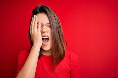 Genç, güzel esmer kız izole edilmiş kırmızı arka plan üzerine gündelik tişört giyiyordu. Yarı yüz, göz ve ağzı elle kapatmaktan bıkmıştı. Yüzüm acıyor..