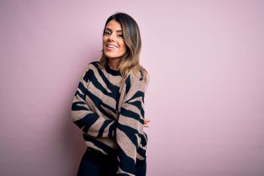 Moda kıyafetleri giyen genç ve güzel bir kadın. Manken, sokak tarzı giyiniyor. Pembe arka planda dikiliyor.