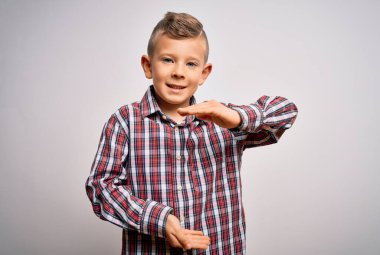 Mavi gözlü, zarif gömlekli küçük beyaz bir çocuk izole arka planda duruyor. Elleri büyük ve büyük boy işareti, ölçü sembolü gösteriyor. Kameraya bakıp gülümsüyor. Ölçüm konsepti.