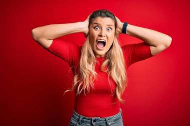 Genç, güzel, sarışın bir kadın. Sıradan bir tişört giyiyor. Kırmızı arka planda dikiliyor.