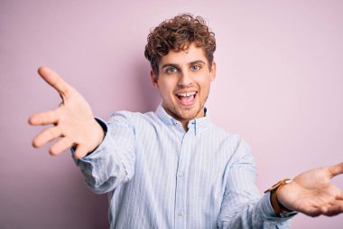 Sarışın, kıvırcık saçlı, beyaz arka planda çizgili tişörtlü, neşeli gülümsemeli, yardım eli uzatan ve kabul gören genç bir adam..