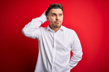 Mavi gözlü, zarif gömlekli genç bir iş adamı kırmızı izole arka planda dikiliyor ve soru sormayı merak ediyor. Şüpheyle kararsız, kafa kafaya düşünerek. Düşünceli kavram.