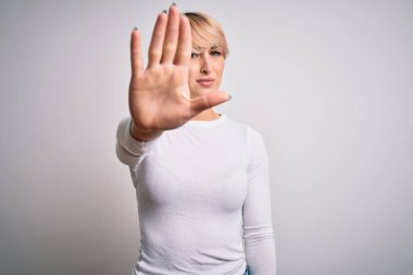 Genç, sarışın, modern kısa saçlı bir kadın izole edilmiş arka planda duruyor ve avuç içiyle şarkı söylemeyi kesiyor. Yüzünde olumsuz ve ciddi bir jest olan uyarı ifadesi.