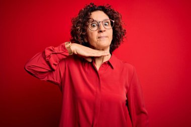 Orta yaşlı, kıvırcık saçlı, rahat gömlekli ve gözlüklü bir kadın kırmızı arka planda boğazını bıçakla kesiyor, saldırganlığı şiddetli bir şiddetle tehdit ediyor.